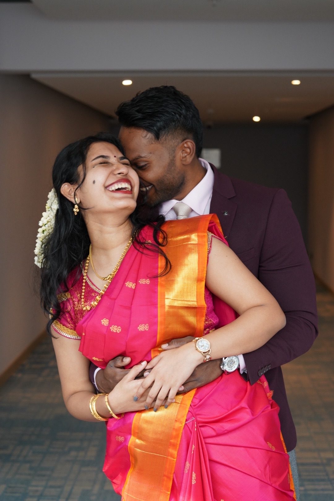 Aster laughing in a pink silk saree as Chris holds her close