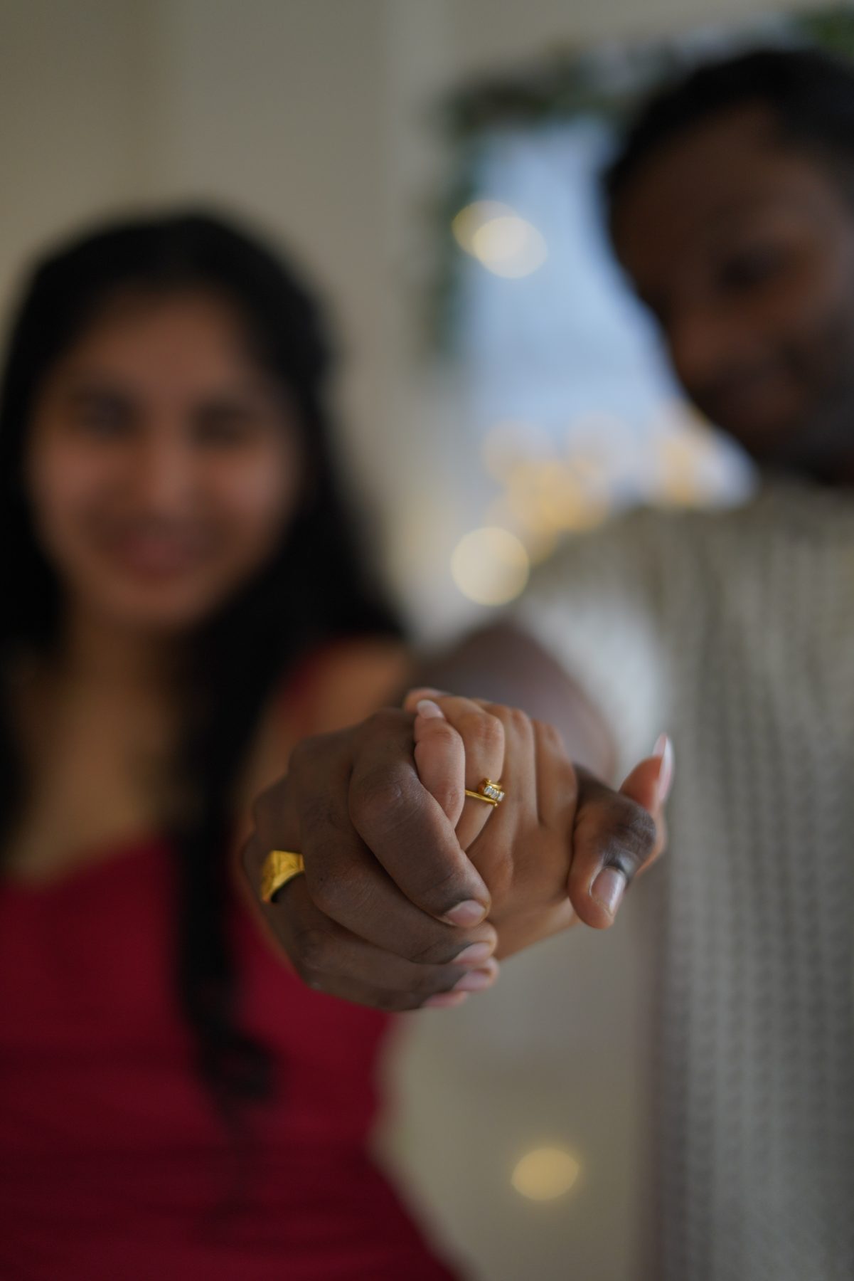 Aster and Chris holding hands toward the camera, the ring between them